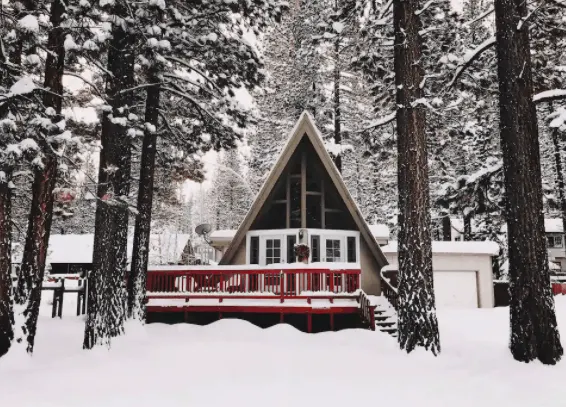 Cabin covered in snow with a red porch in the woods