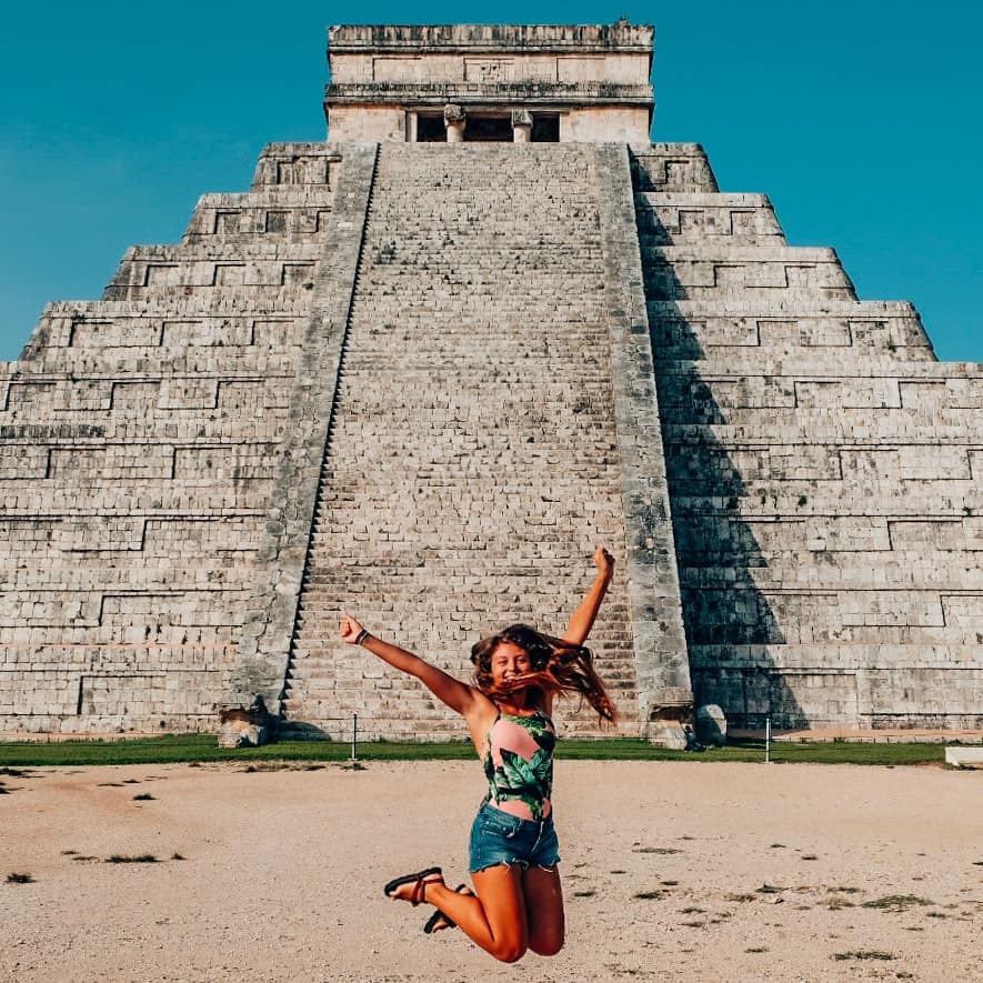 a girl jumping in front of Chichen Itza 