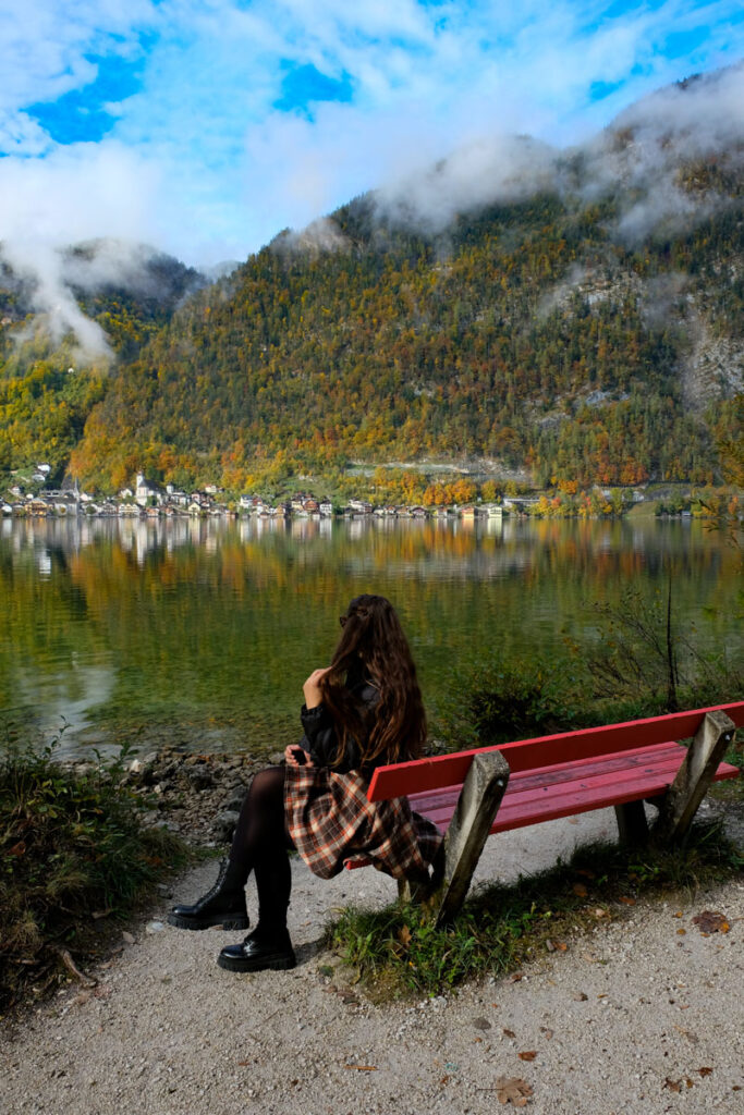 girl sitting on a bench with a view of hallstatt across the lake