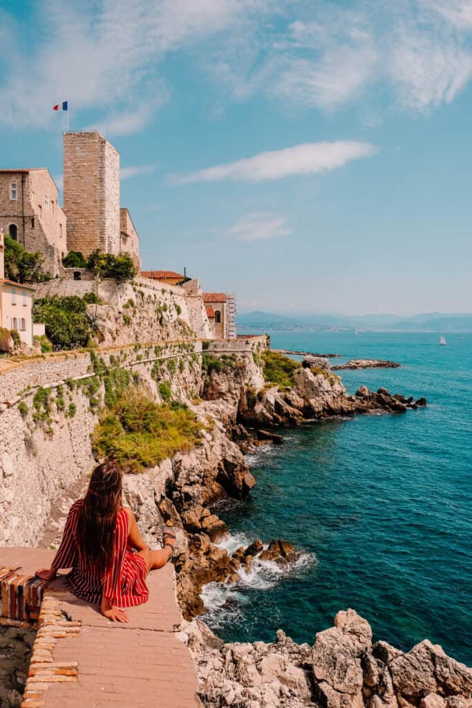 A woman sitting on a seaside walkway below the old town walls of Antibes
