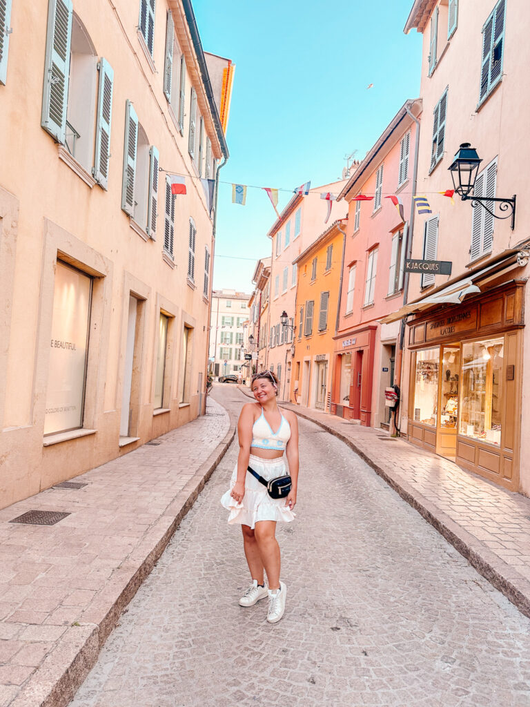 A woman in a white outfit standing in a pastel street in Saint-Tropez