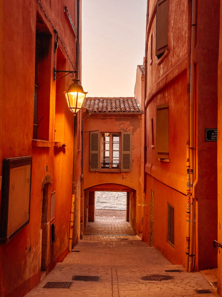 A narrow orange alley in Saint-Tropez with an archway opening onto the sea