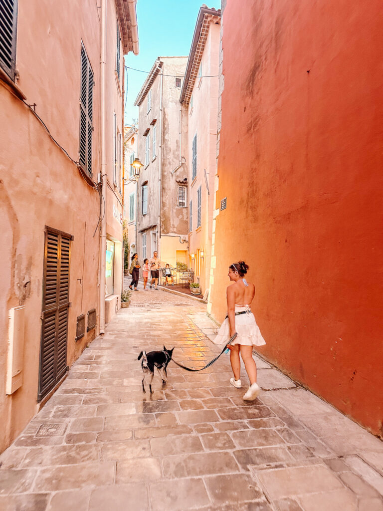 A woman walking a small dog down a narrow orange street in Saint-Tropez